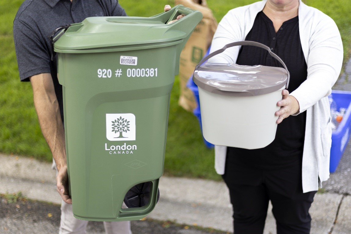 Two people standing holding a green bin and kitchen catcher