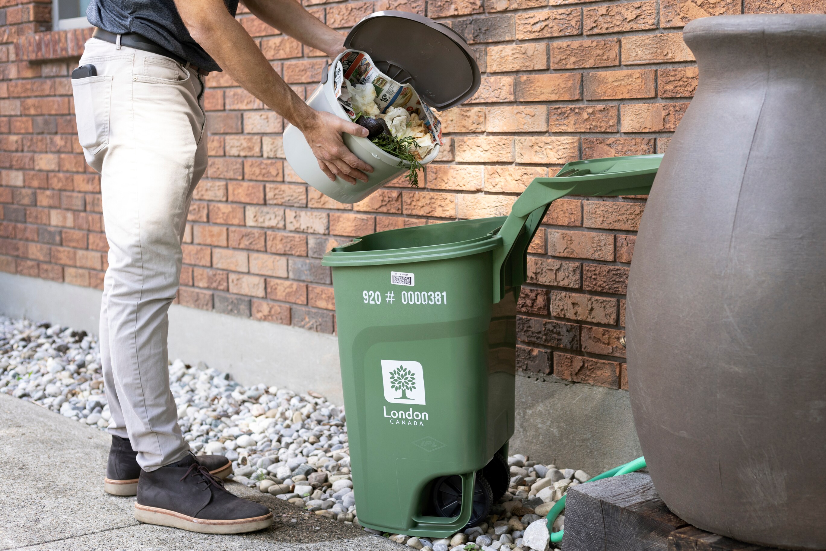  A man empties the materials from a Kitchen Container into an open Green Bin. 